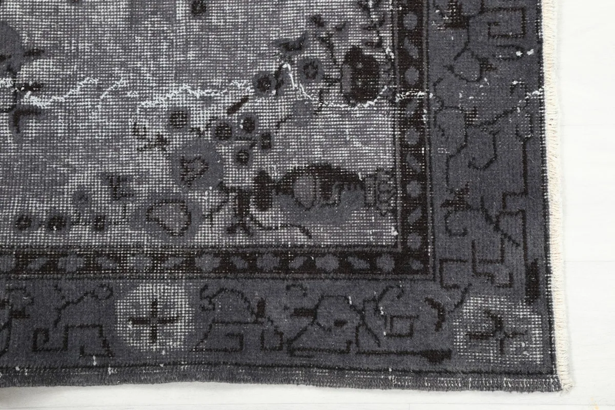 Corner detail showing the charcoal border design and the subtle gray field of the rug