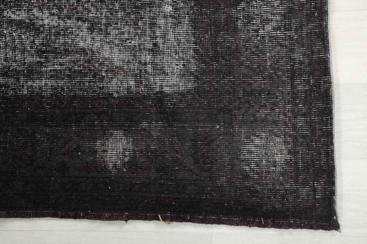 Detail of the rug's corner, showing the faded charcoal pile and subtle wear.
