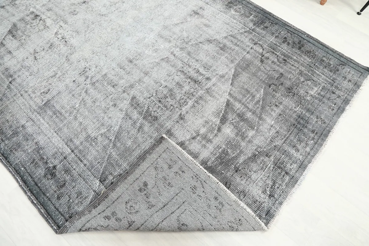 Corner of the gray rug folded to reveal the cotton foundation and reverse side of the knotting
