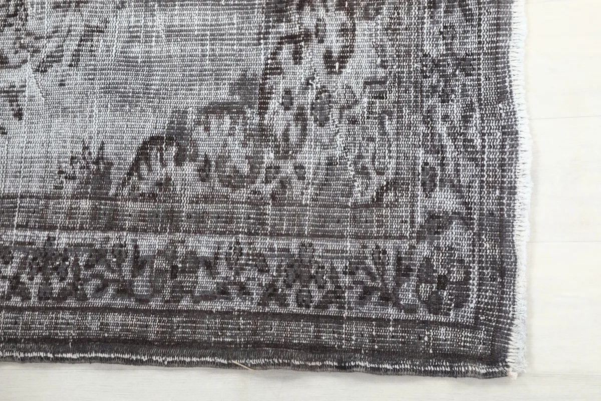 Detail of the rug's charcoal border design and the distressed texture of the wool pile.