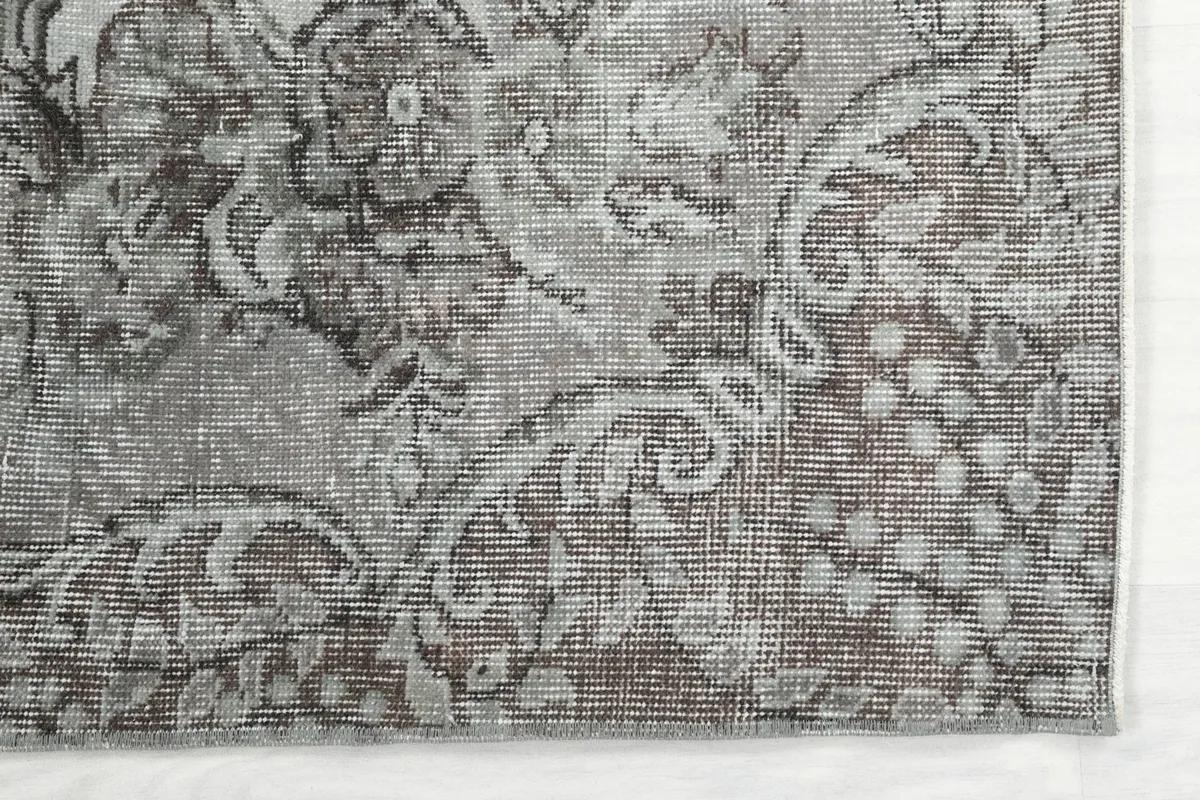 Detailed view of the distressed gray and beige wool pile and intricate floral patterns on the rug