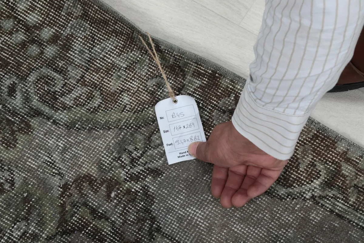 Hand holding a product tag on the rug, showing the texture and vintage condition of the pile