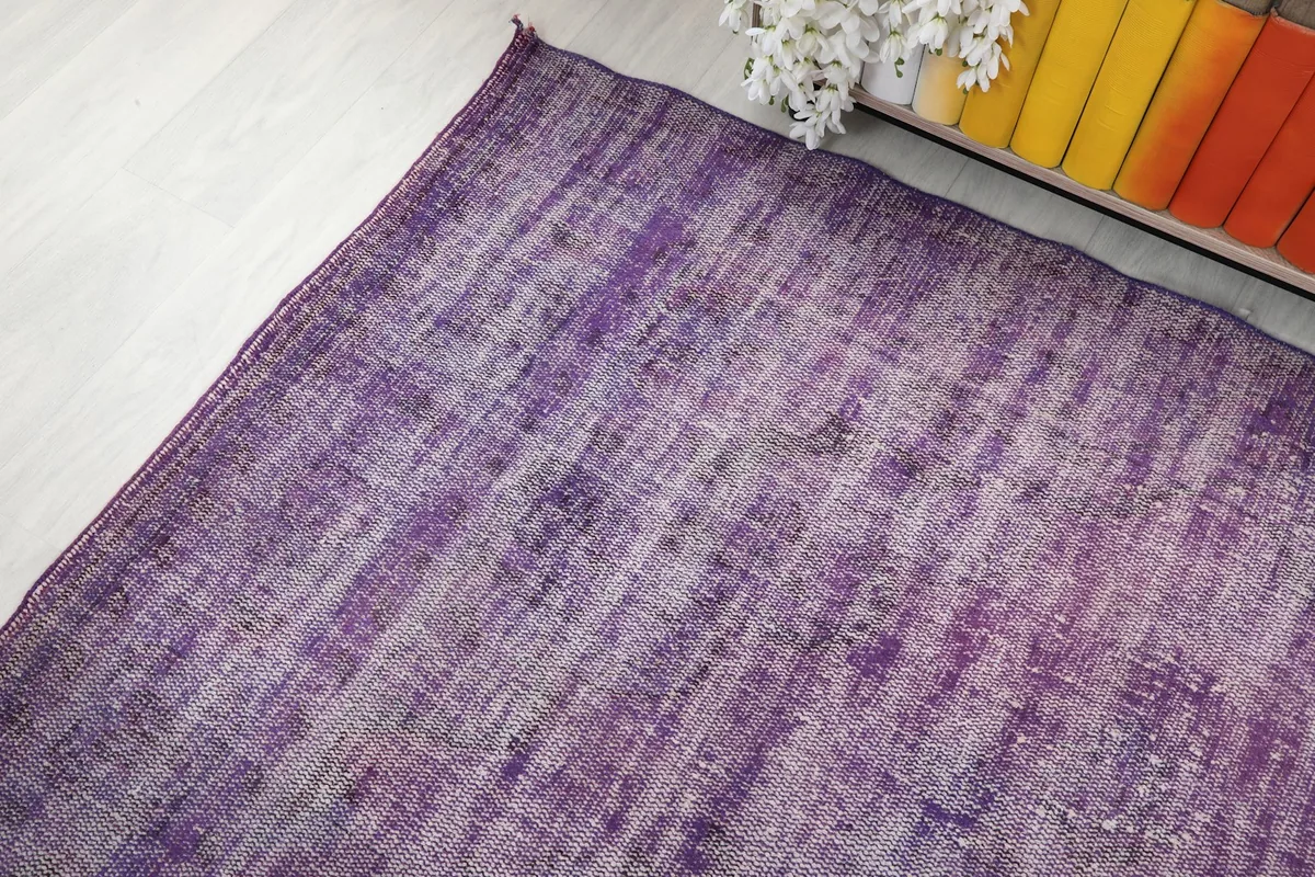Corner view of the purple rug extending towards a bookshelf with colorful books