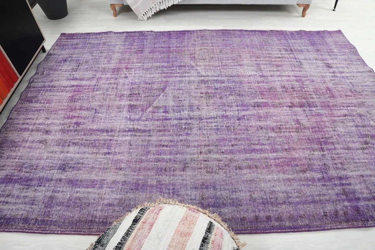 Overhead room view of the purple rug, positioned in front of a sofa and decorative pouf