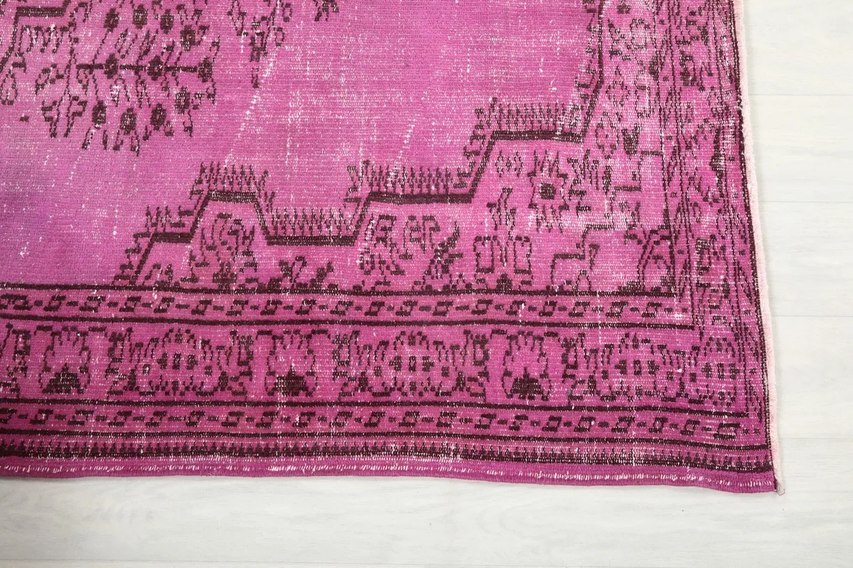 Detail of the rug's border, showcasing geometric patterns in dark brown on pink