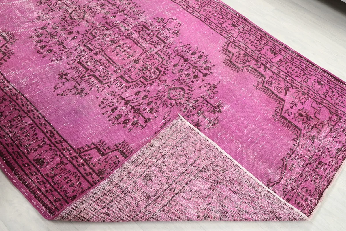 Corner of the pink rug folded back, revealing the reverse side of the hand-knotted construction
