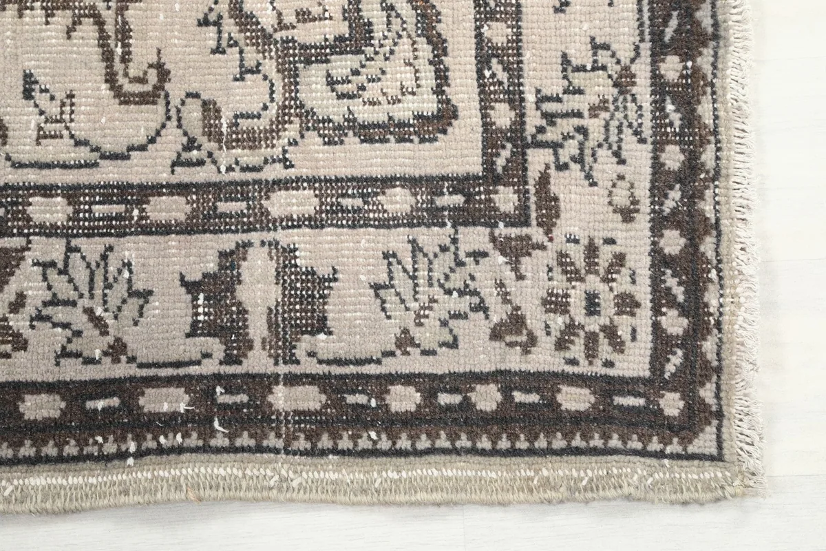 Close-up of the rug's corner showing floral and geometric motifs in beige and charcoal