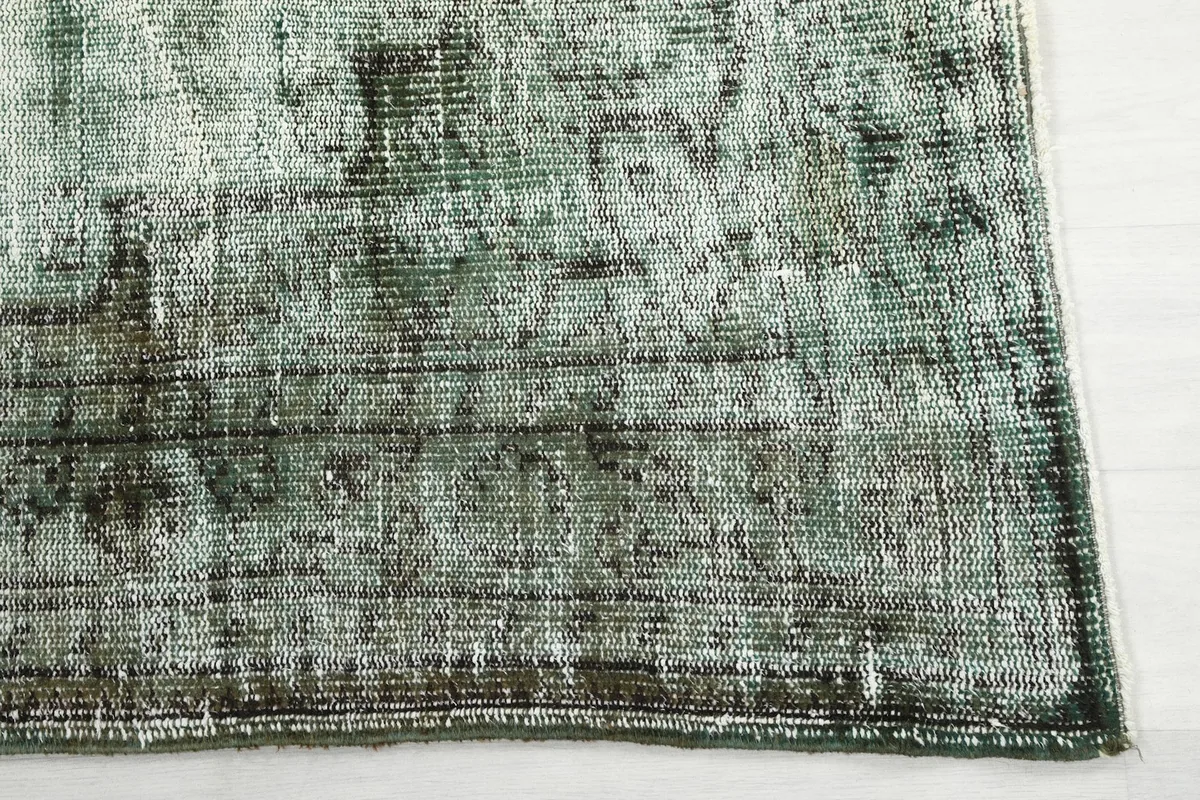 Detail of the rug's corner and border, showing the faded patterns and subtle color variations.