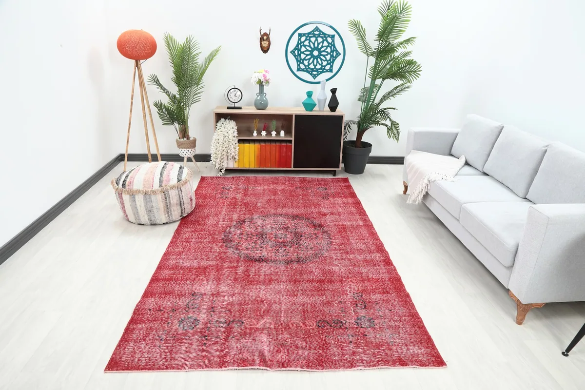 Red vintage Anatolian rug displayed in a living room setting with a light gray sofa.