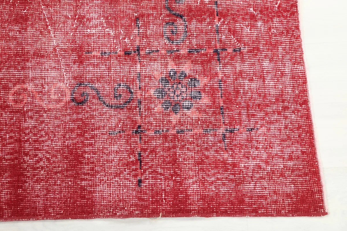 Detail of the rug's red field with faded charcoal geometric and floral elements near the corner.