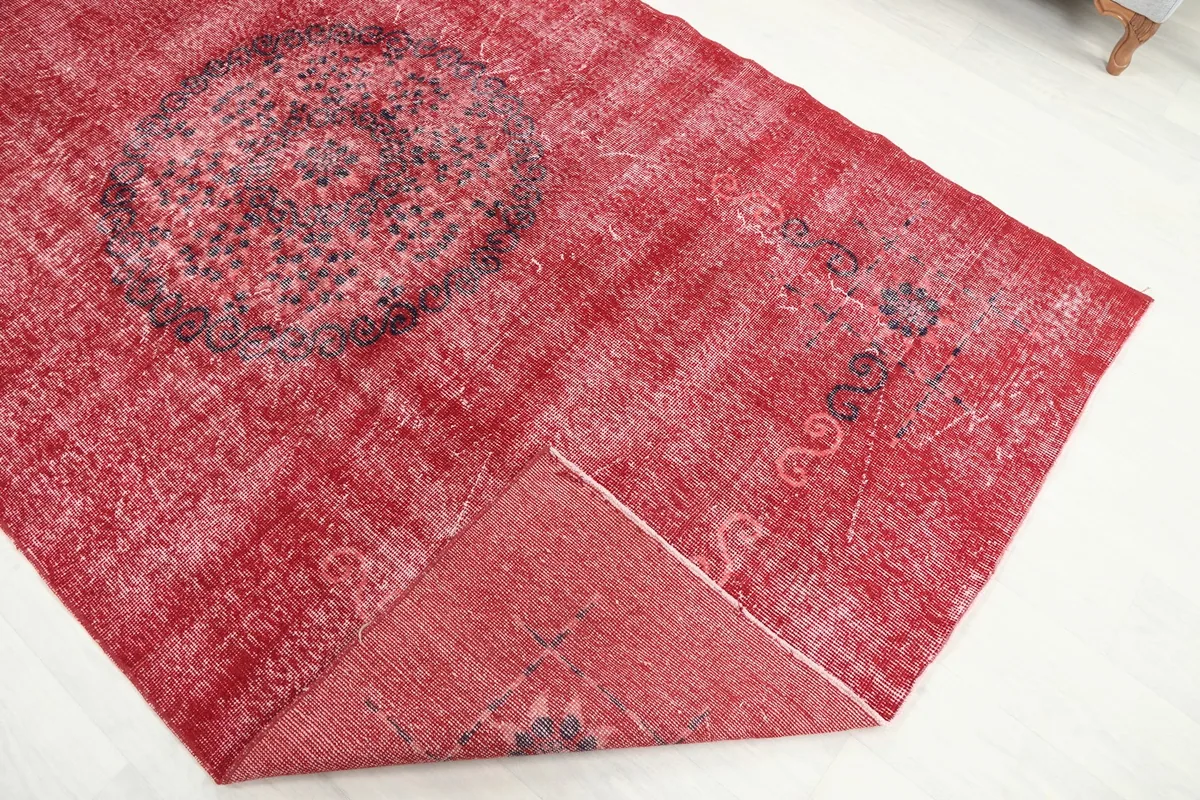 Corner of the red vintage rug folded back, revealing the reverse side and hand-knotted cotton foundation.