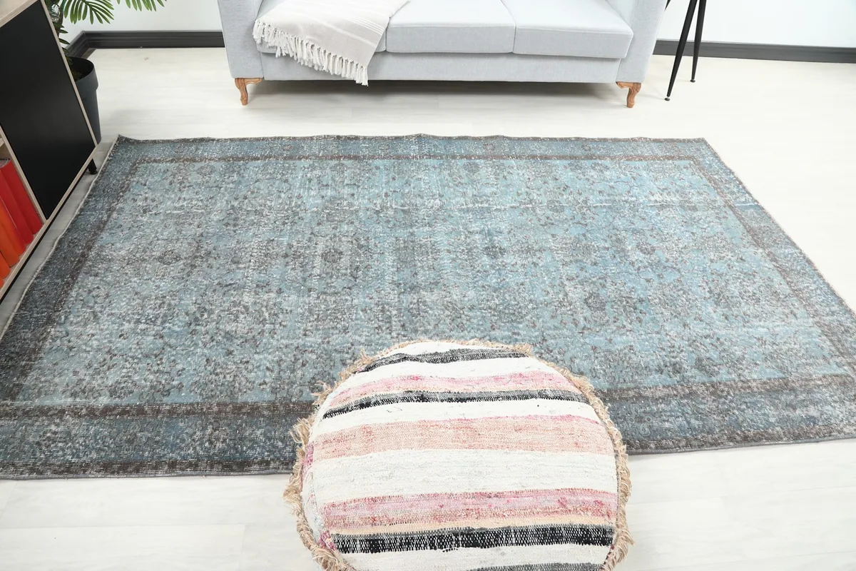Wide room view of the blue rug with a pouf in the foreground, showcasing its full length