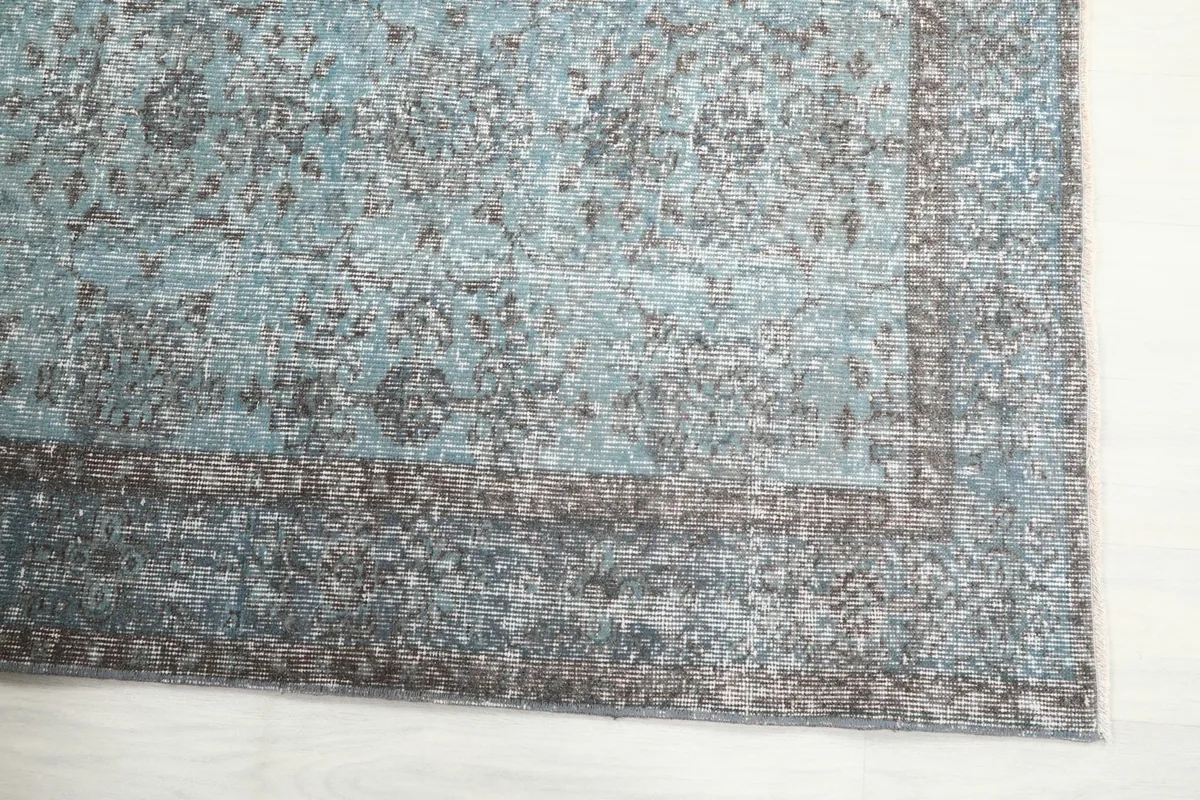 Detailed view of the corner of the blue rug, highlighting faded floral patterns and border