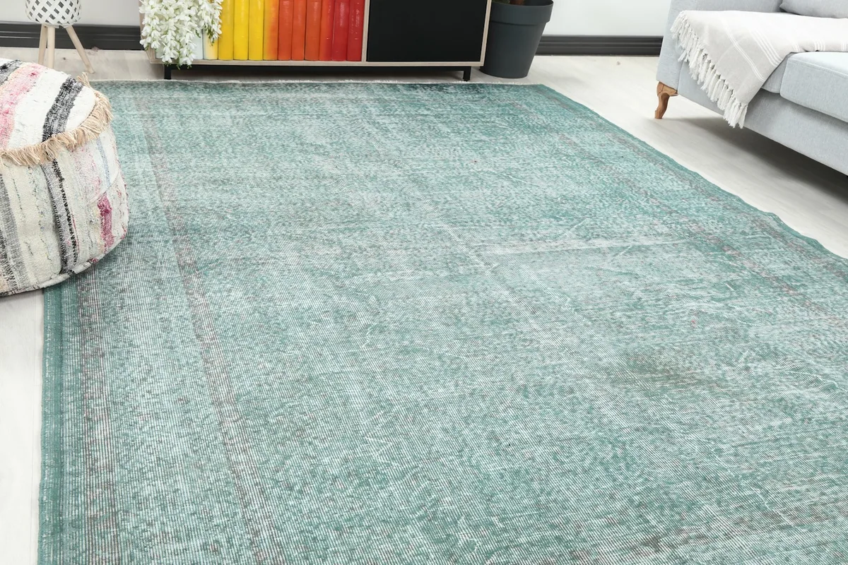 Close-up angle view of the distressed green rug's surface and faded geometric patterns.