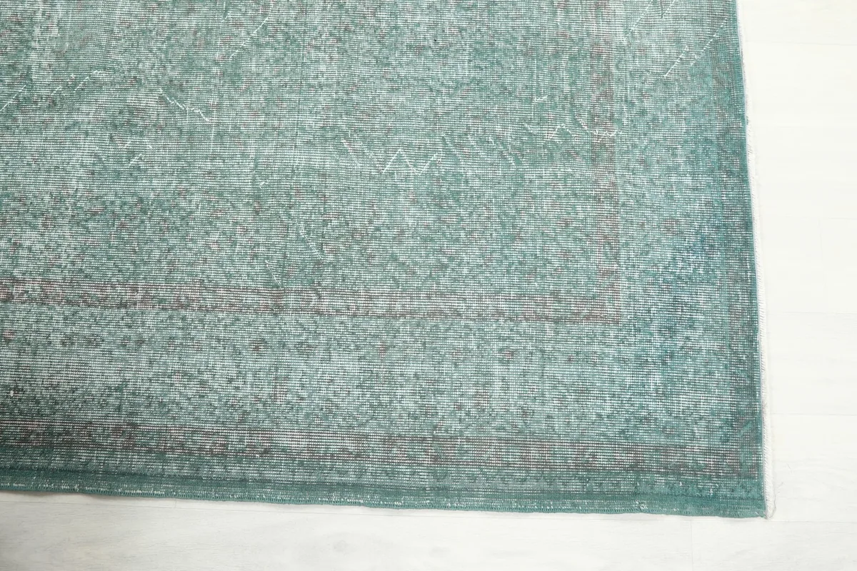 Detail of the rug's corner, showing the subtle border design and distressed green color.