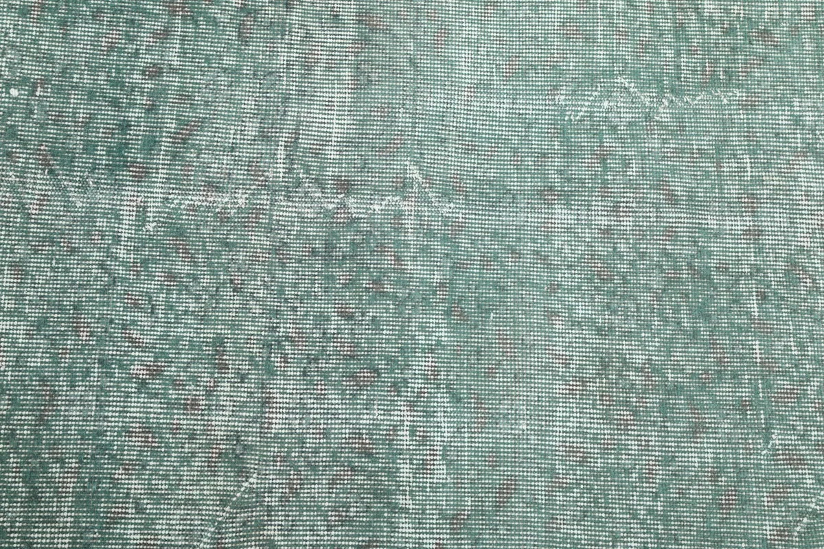 Close-up of the low pile texture and distressed wool fibers of the green vintage rug.