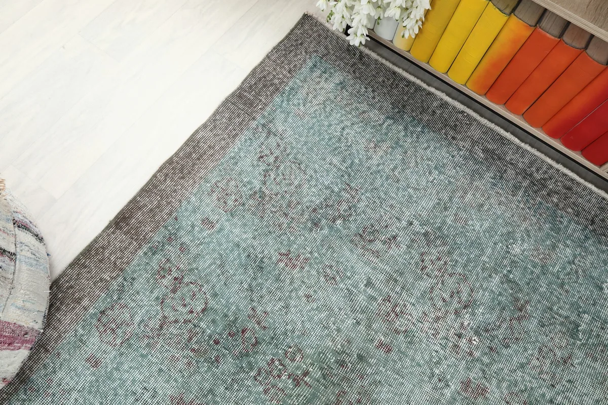 High-angle shot focusing on a corner of the rug, next to a cabinet with colorful books.