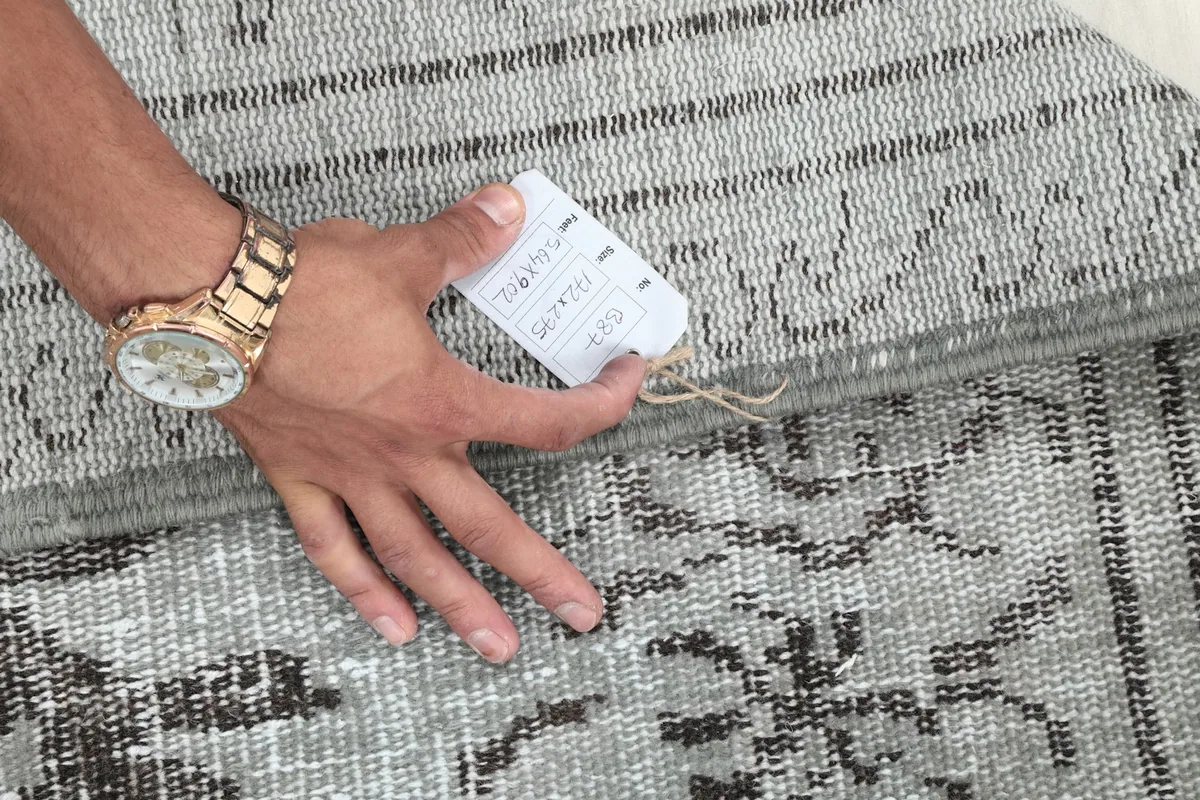 Hand holding a tag, indicating the rug's authenticity and vintage origin.