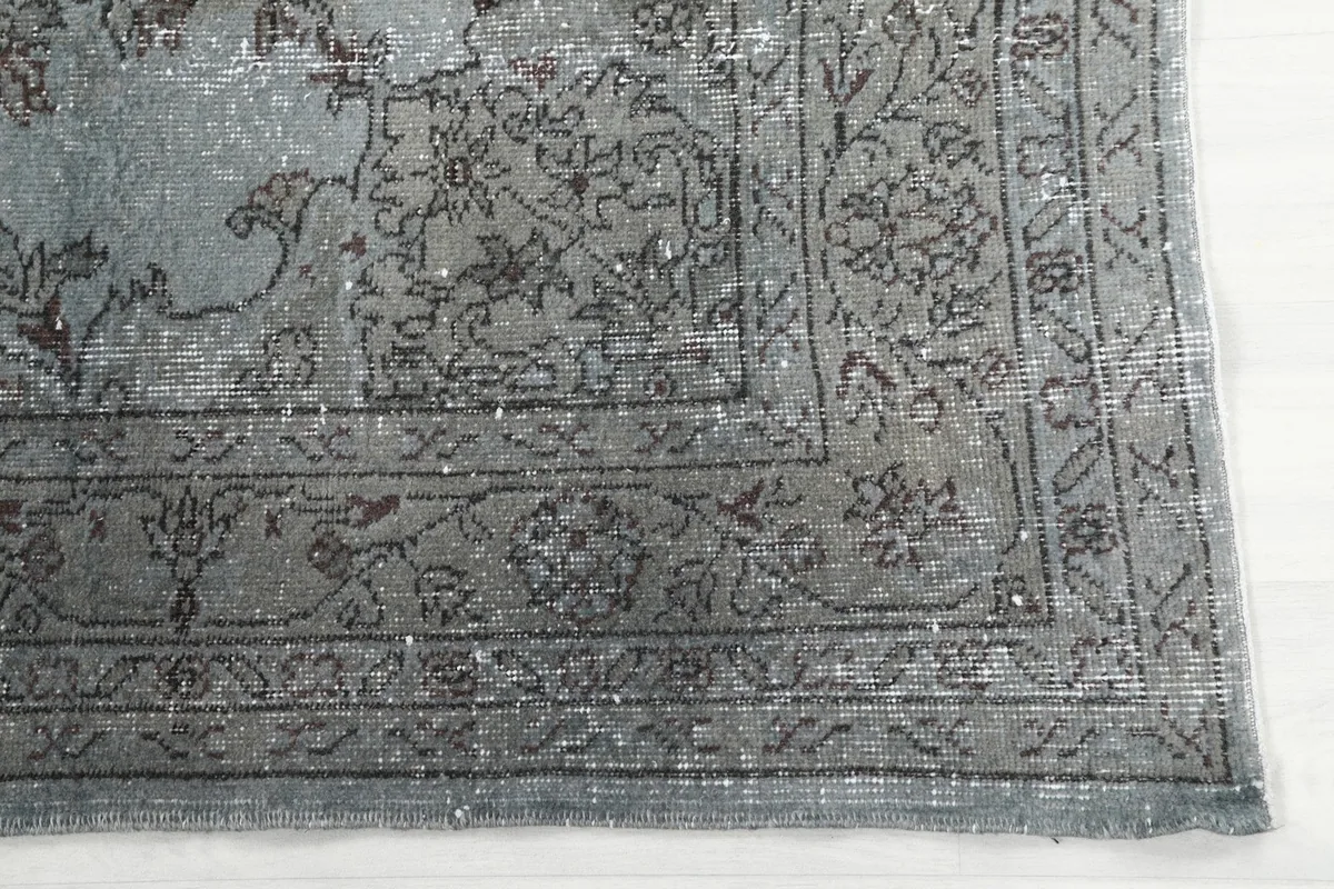 Detail of the intricate floral border design in gray on the blue vintage rug