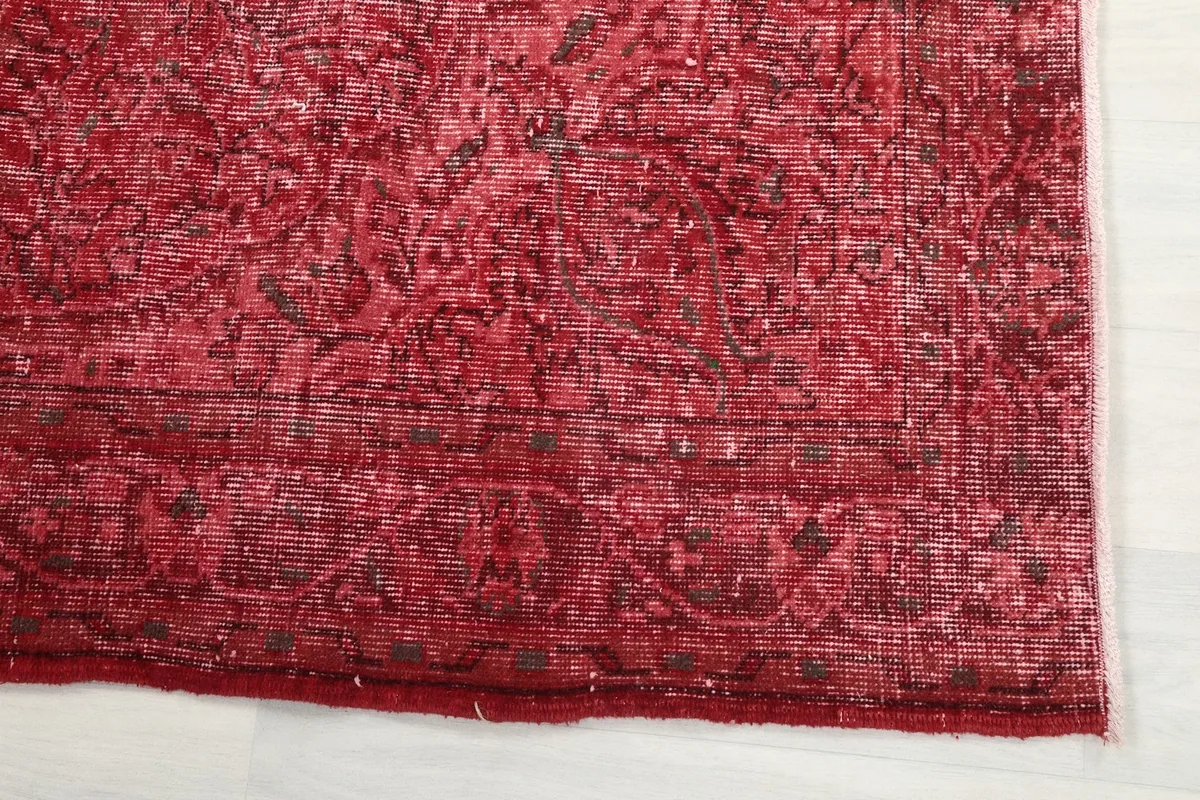 Detail of the rug's border, showing the faded red tones and intricate, worn patterns.
