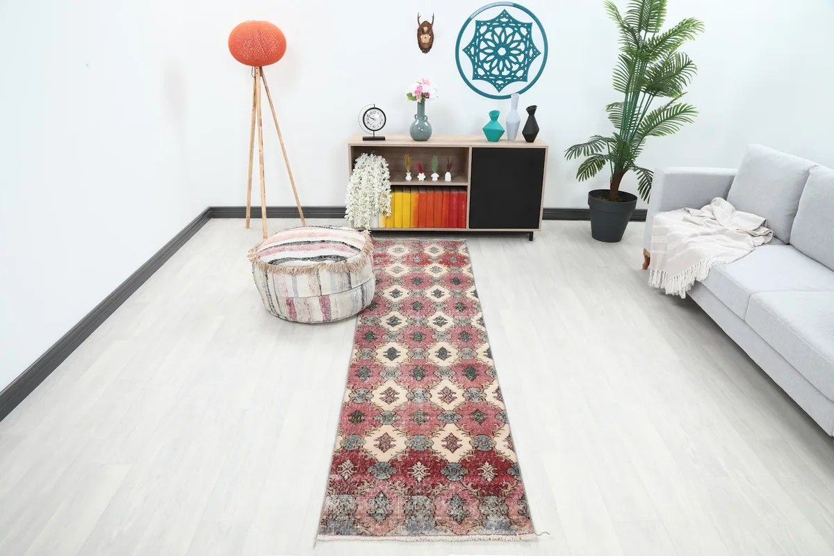 Vintage runner rug displayed in a bright living area, extending from a pouf towards a gray sofa.