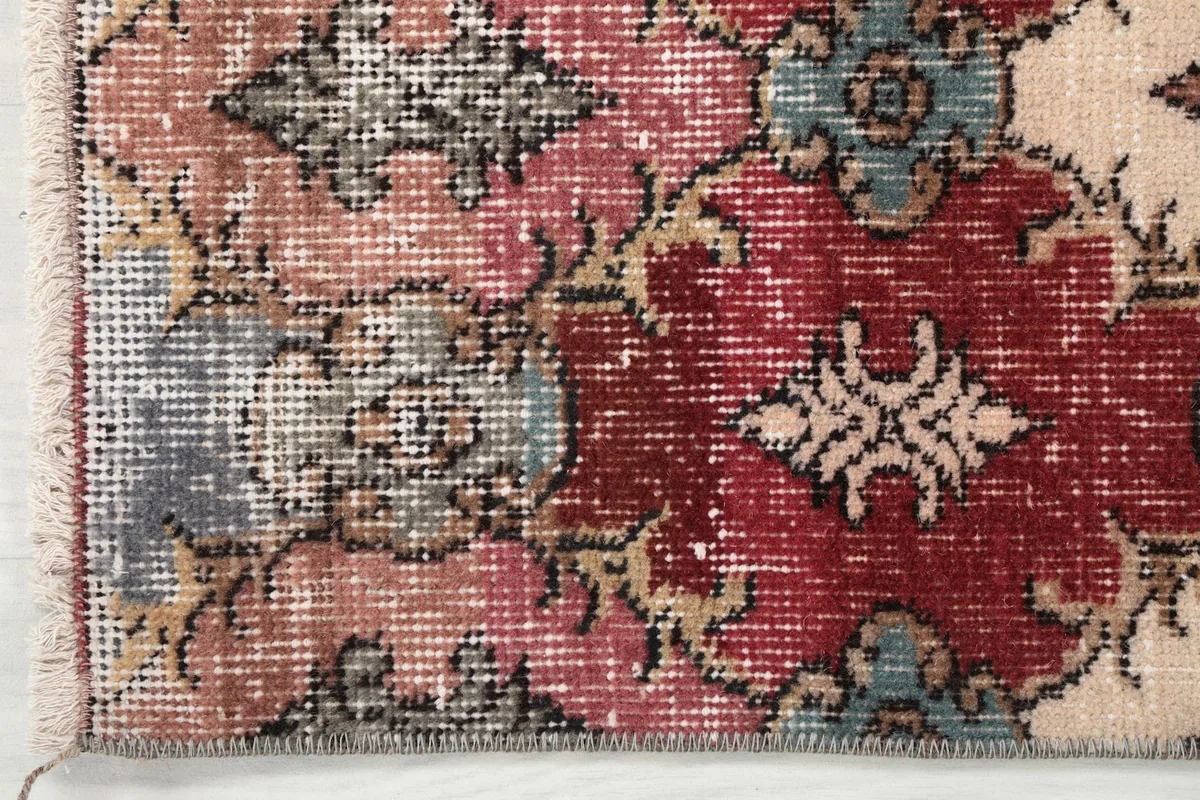 Detail showing the edge and a section of the rug with its rose, red, and gray geometric designs.
