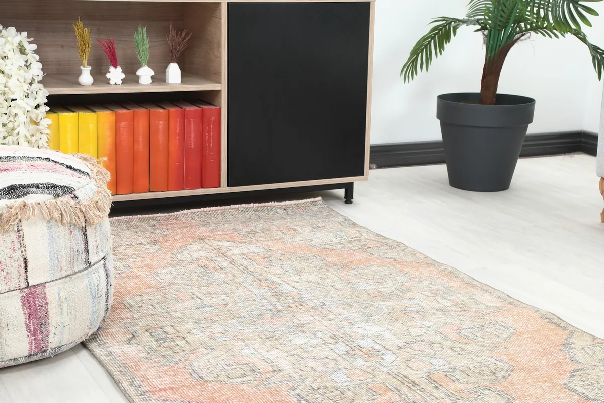 Close-up view of the vintage rug's texture and colors next to a wooden cabinet and pouf.