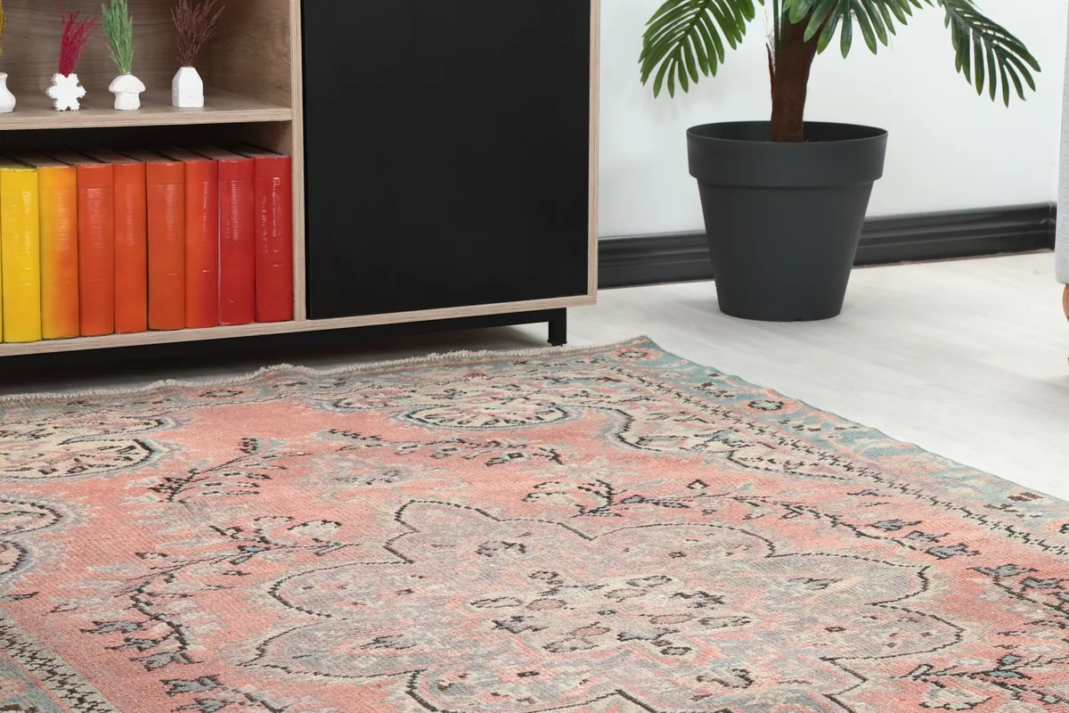 Close-up angle showing the rose field and blue border of the vintage rug next to furniture