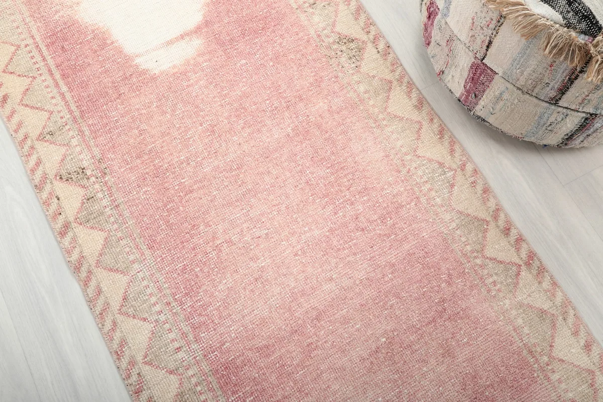 Detailed view of the rose pink field and the beige geometric border of the hand-knotted runner.