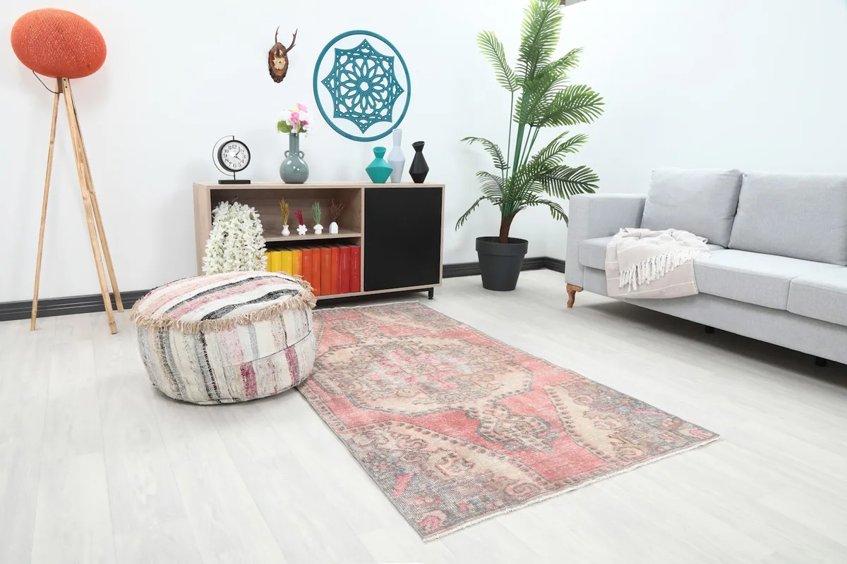 Angle view of the rose and beige Anatolian rug in a room, showing its placement next to a pouf and sofa.