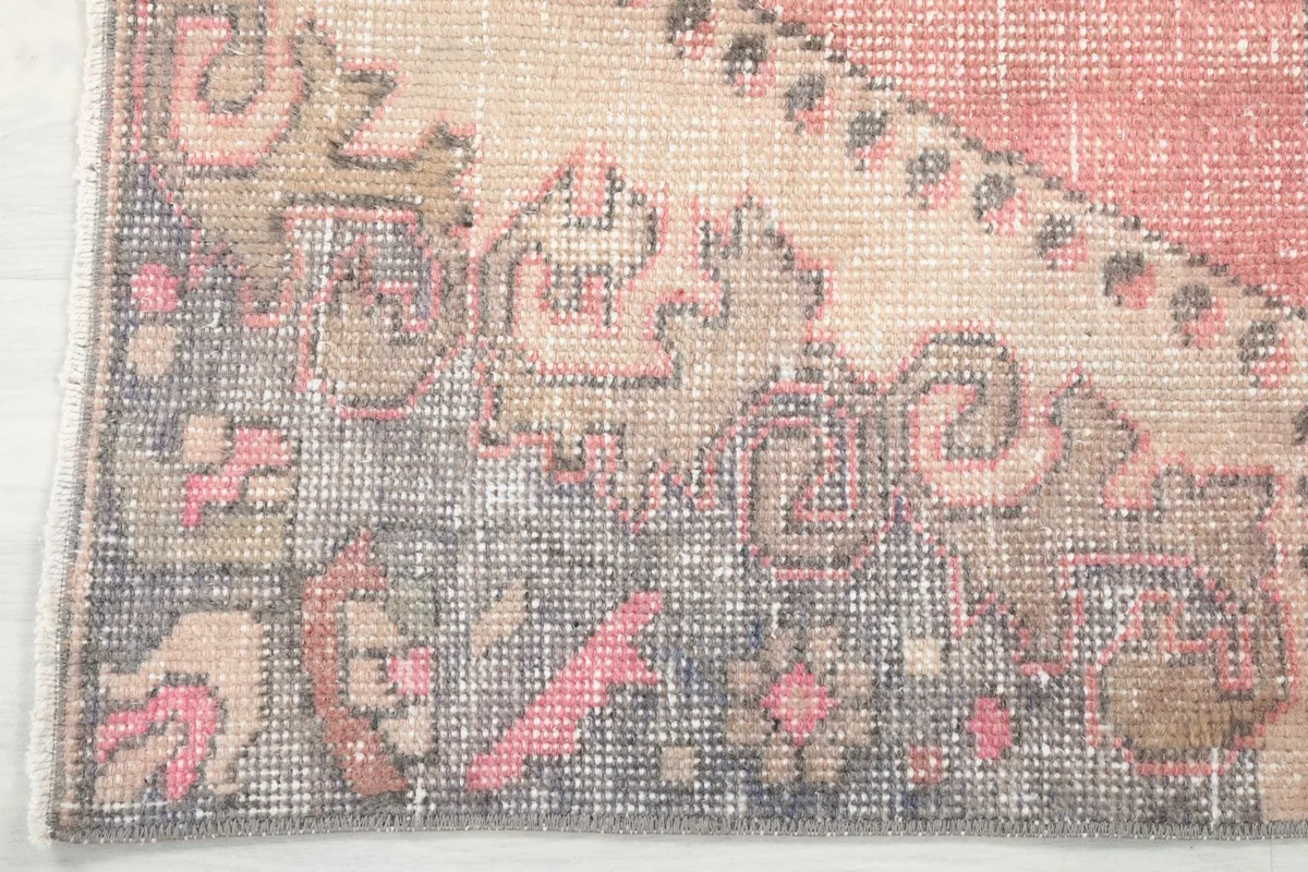 Close-up of the rug's border, showcasing the gray and brown tones with subtle rose accents and wear.