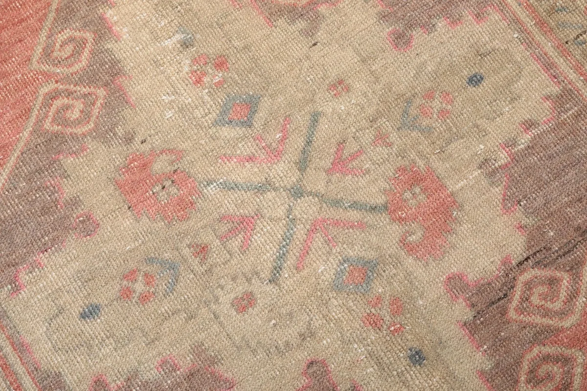 Detailed view of the central geometric motif showing faded rose, beige, blue, and gray colors