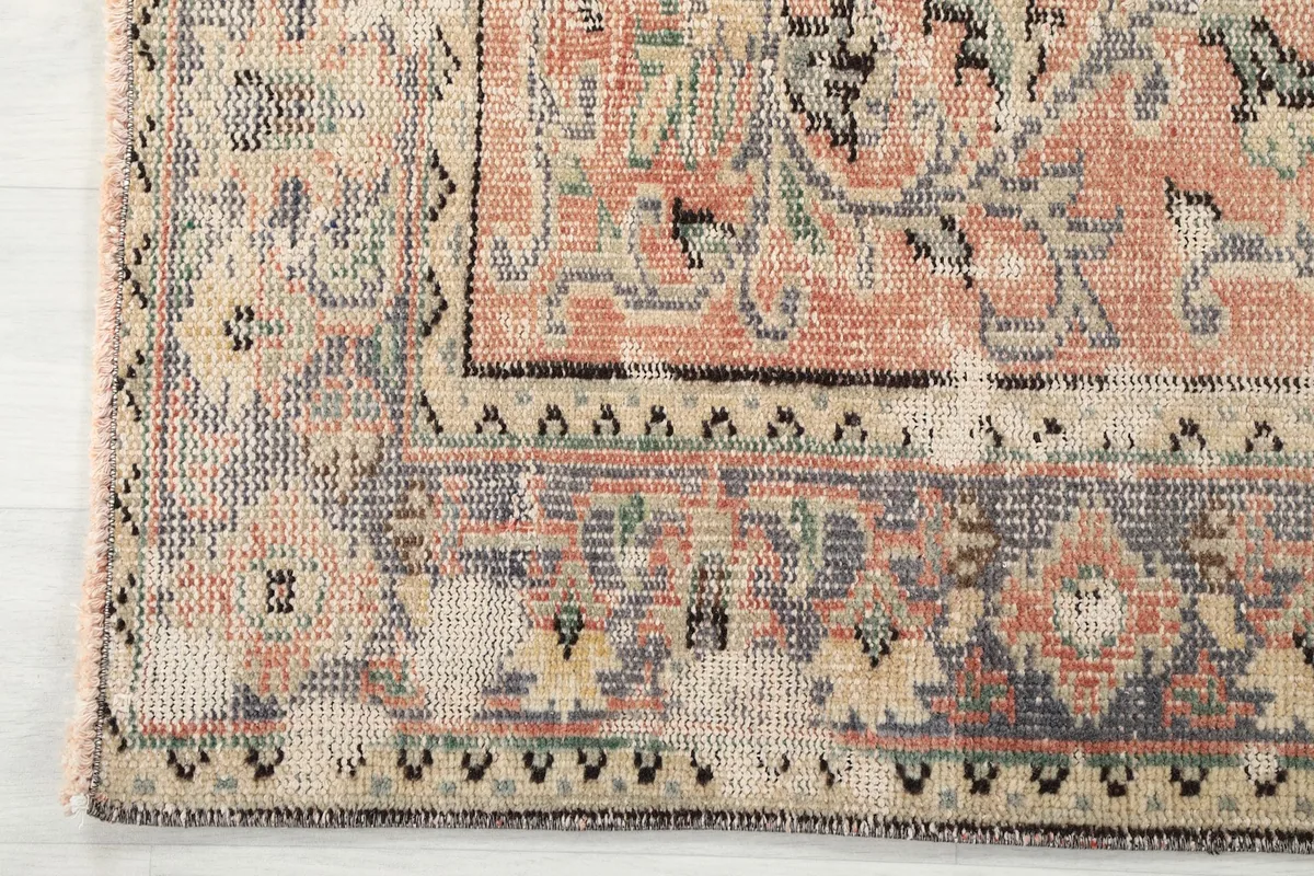 Corner detail of the rug, showing the distressed gray border with geometric patterns and fringe
