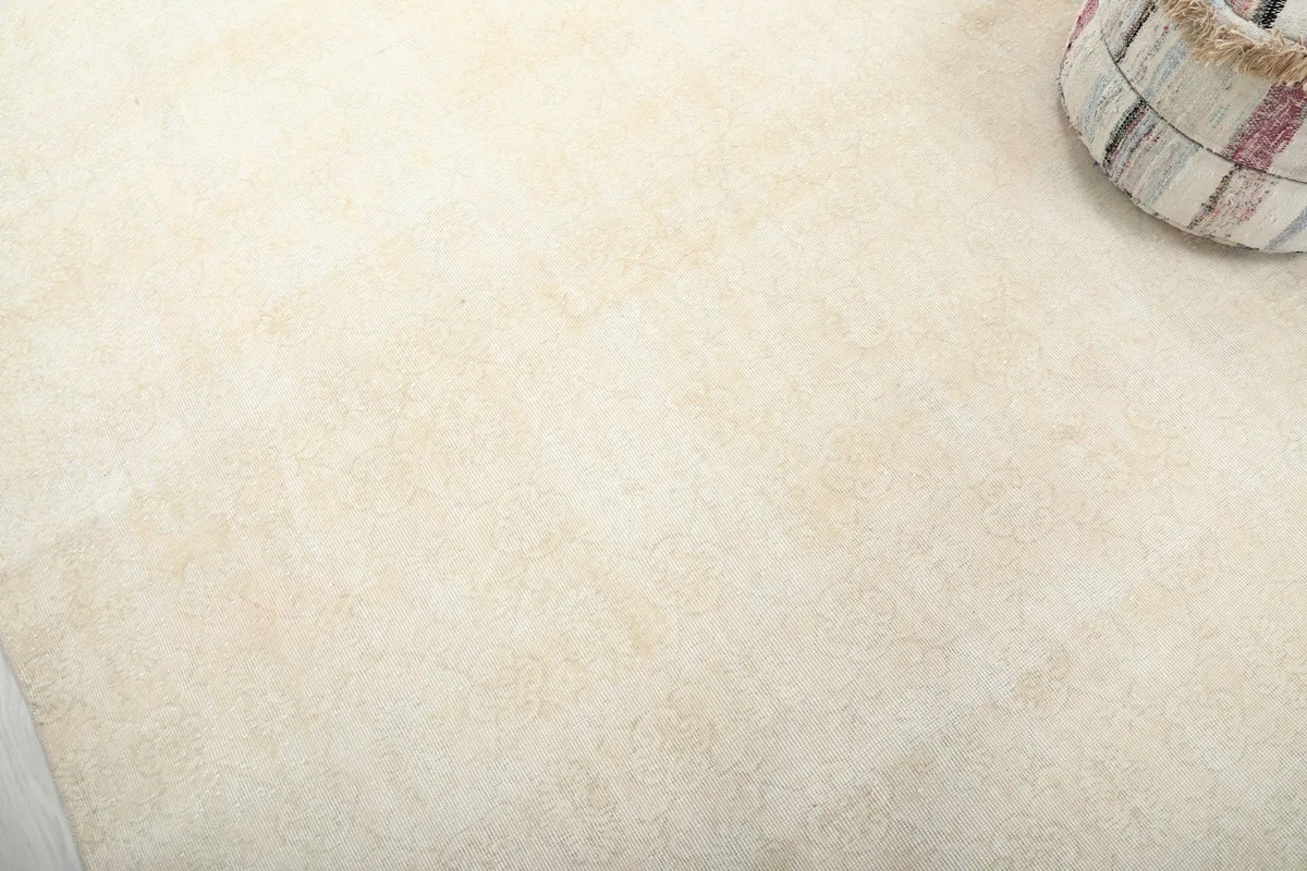 Close-up of the vintage ivory rug's low pile and faded, subtle floral patterns