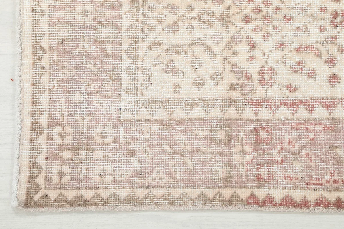 Close-up of the vintage rug's rose-toned border with geometric details and fringe
