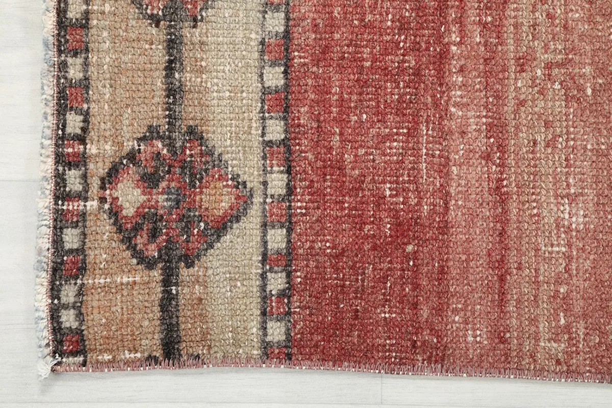 Edge of the runner rug showing the beige border and the faded rose main field