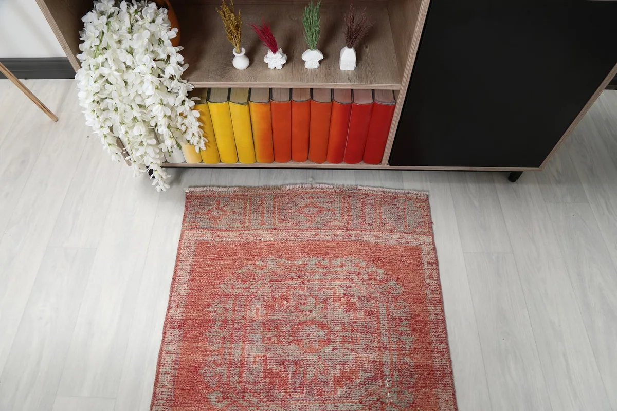 Overhead detail of one end of the soft rust runner rug, showing the faded patterns near a bookshelf