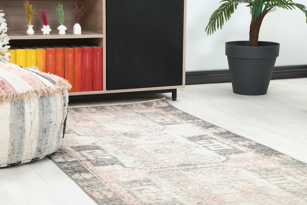 Close-up of a section of the runner rug in a room, next to a striped pouf and bookshelf.