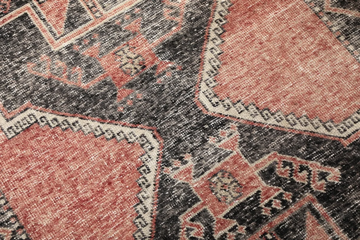 Detailed close-up of the hand-knotted wool pile, showing the rust and charcoal colors and wear