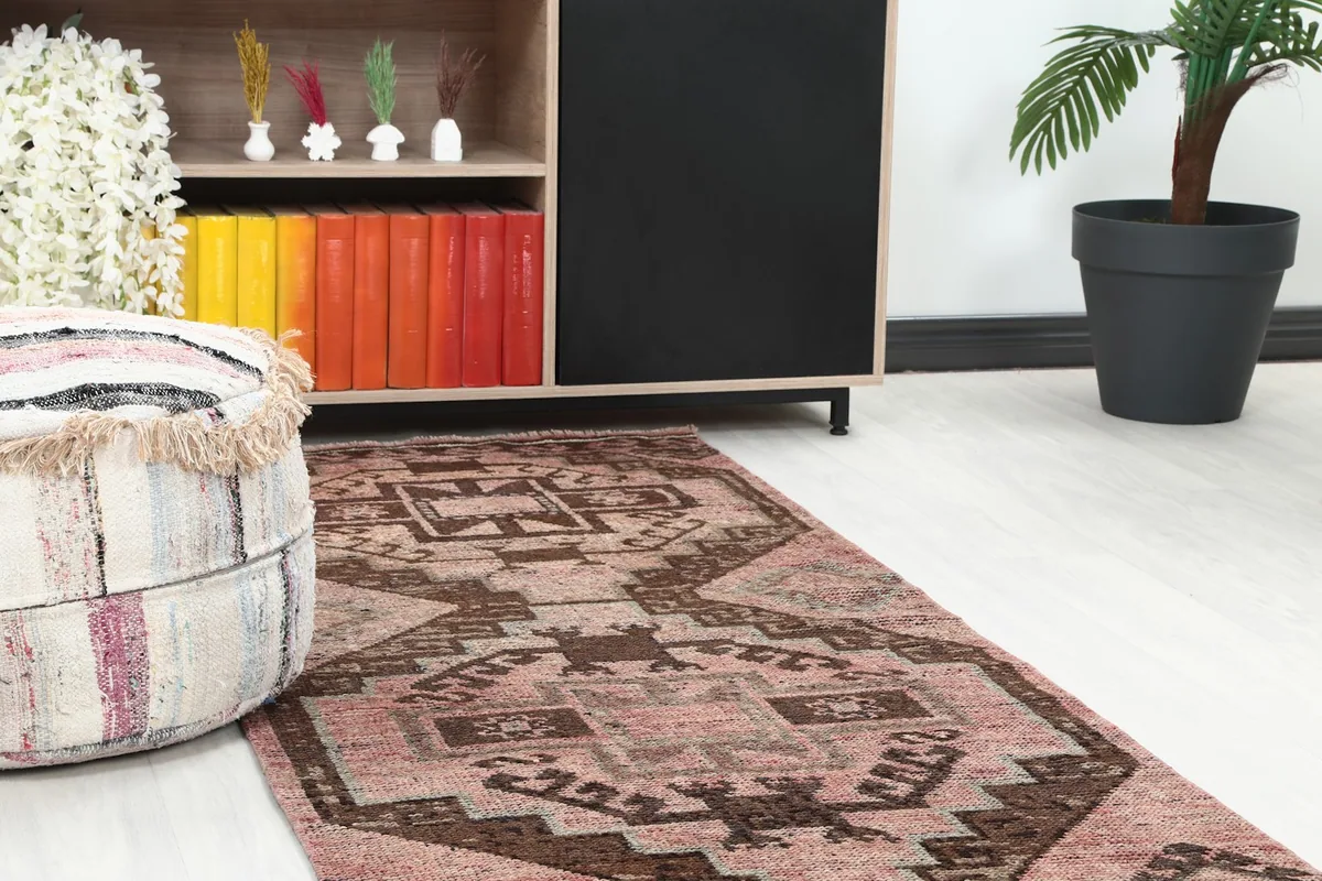 Close-up of the runner rug's pattern next to a brown ottoman and bookshelf in a room