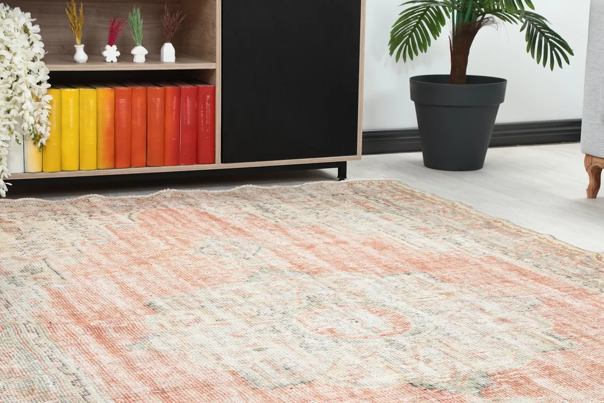 Close-up of the vintage rug's corner near a wooden cabinet with colorful books and a plant