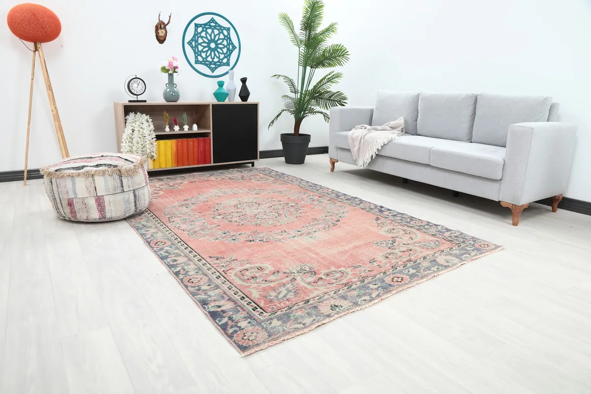Faded rose area rug placed in a living space, showing its scale relative to a sofa and ottoman.