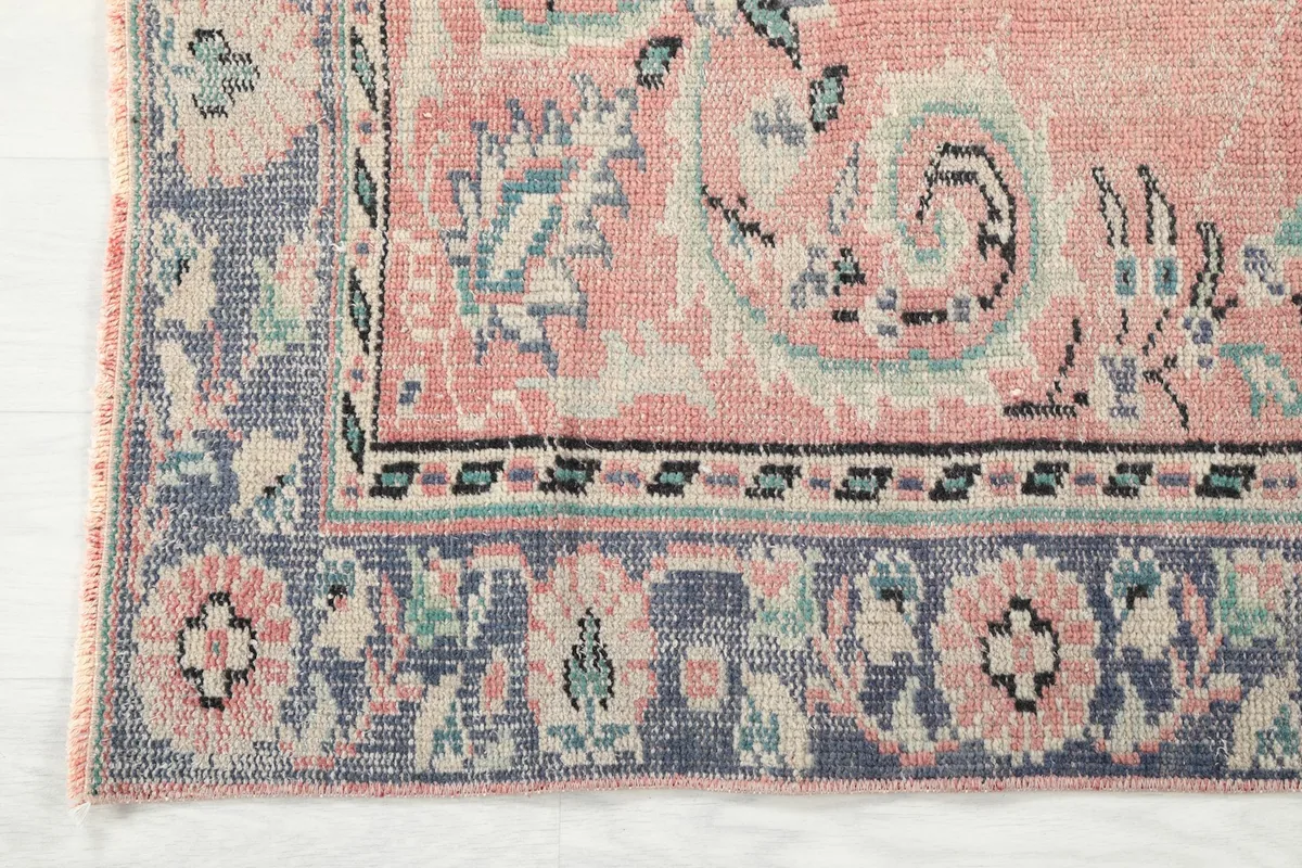 Detailed shot of the rug's corner, showing the navy border with floral patterns and the faded pile.