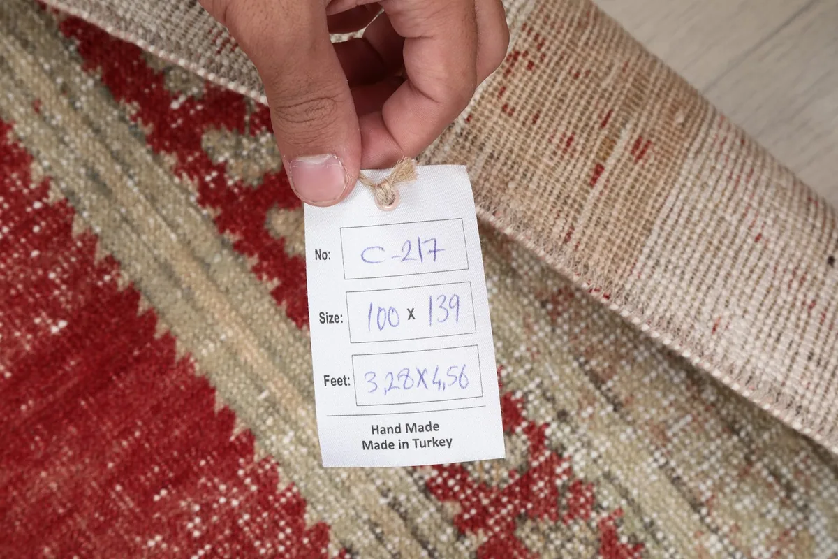 Hand holding the product tag, displaying the rug's dimensions and origin as hand-made in Turkey.