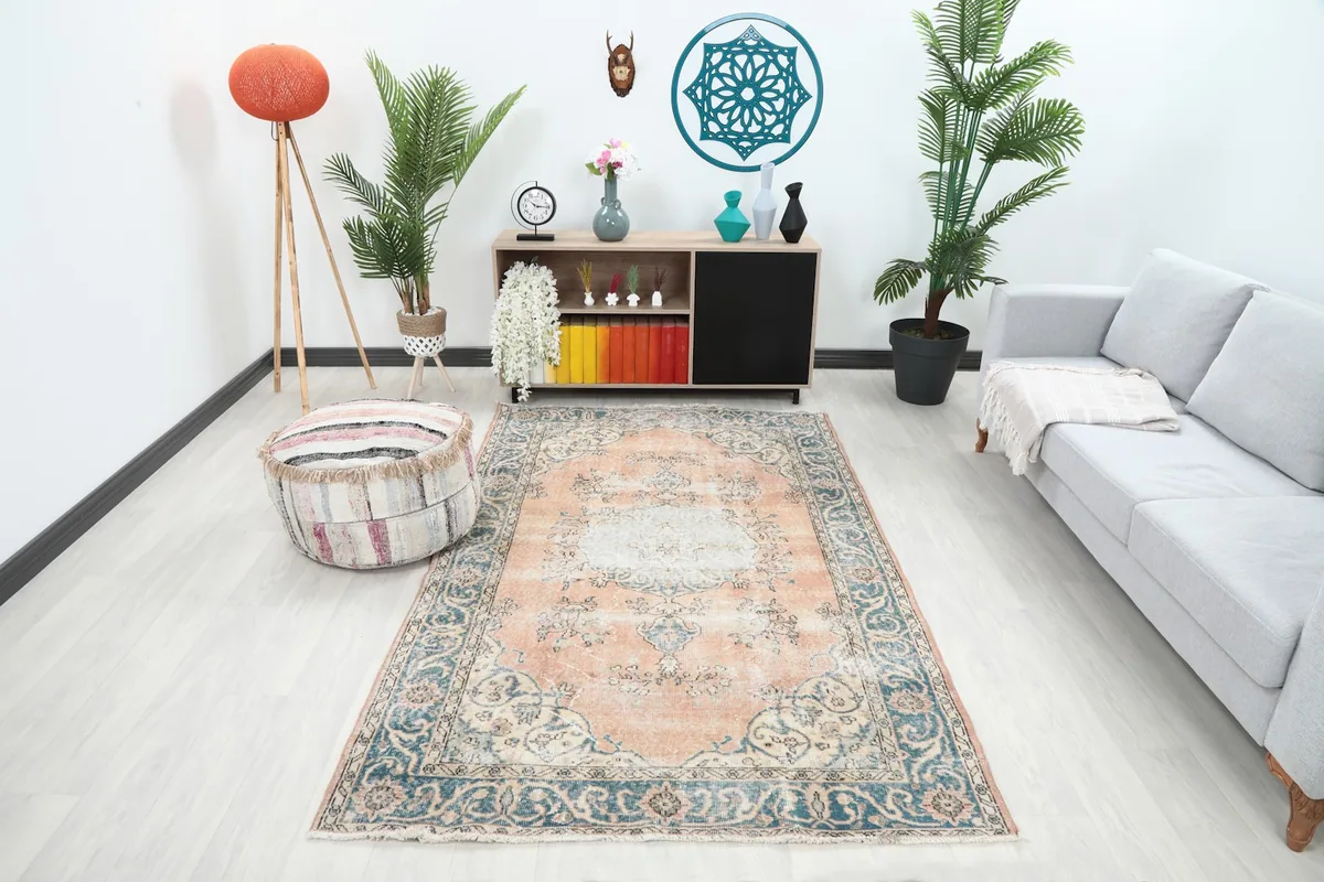 Vintage rust and blue rug placed in a living room setting with a light-colored sofa and ottoman.