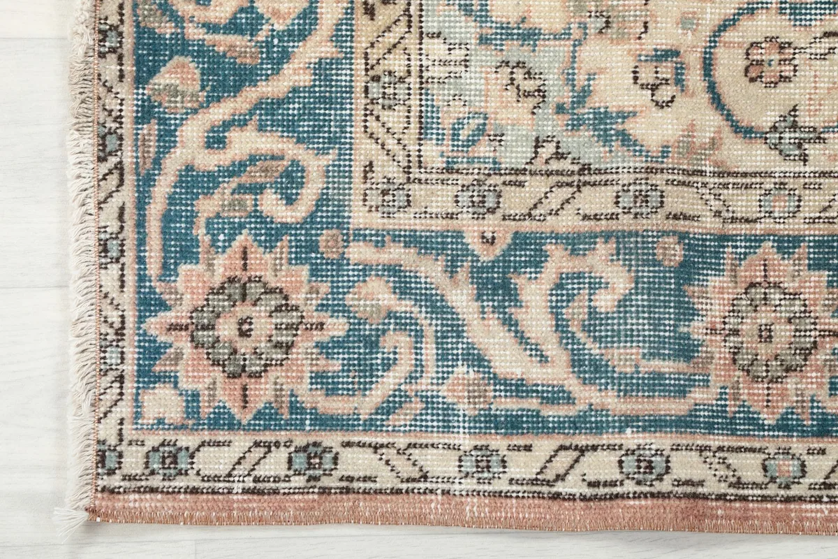 Detail of the rug's blue border with decorative floral elements and the rust edge.