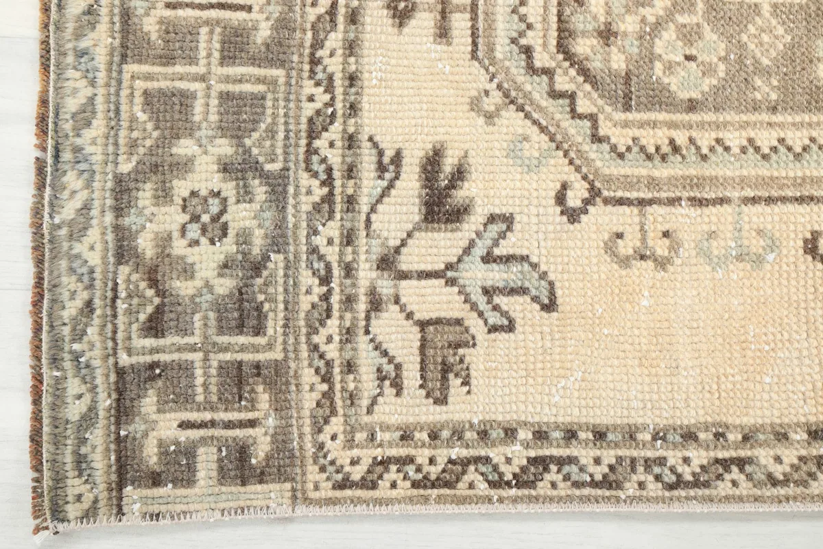 Detailed shot of the rug's border design, showcasing the brown geometric motifs and the beige field