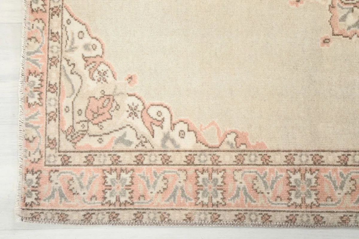 Detailed shot of the rug's border design and corner with muted rose and gray tones