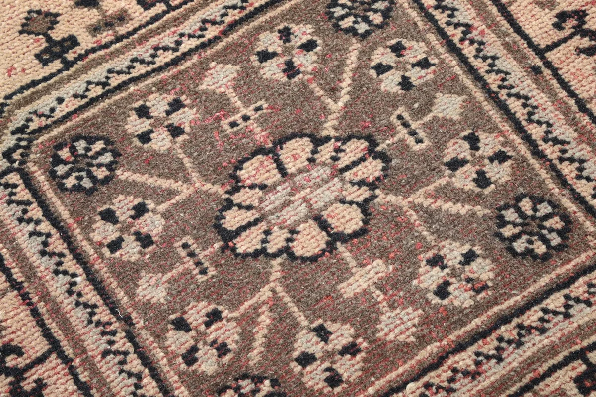 Detailed close-up of a central geometric panel with floral-like elements in black and brown on the tan rug.
