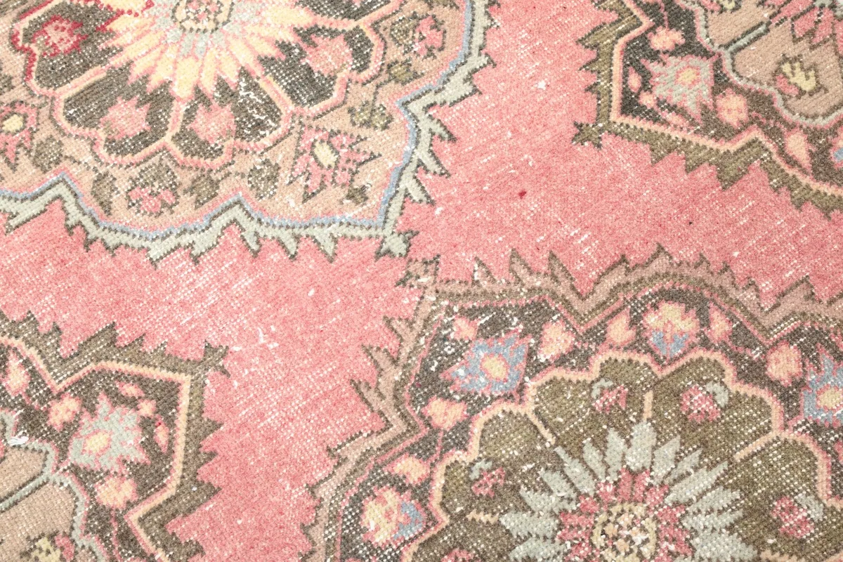 Detailed close-up of the rug's surface, showing the faded pink and red hues and medallion details